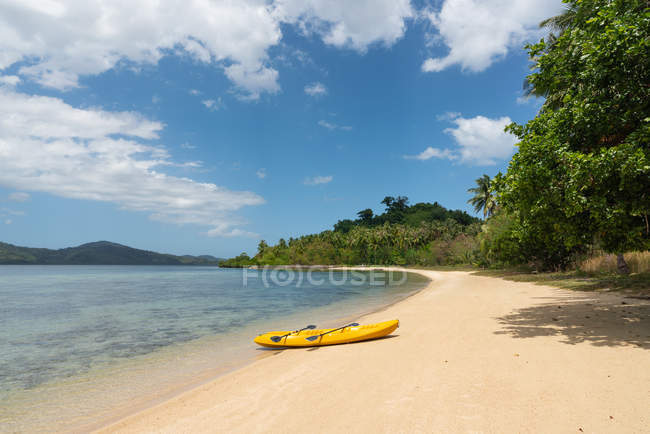 Canoa amarilla vacía en la playa de arena de la isla tropical en el fondo de la selva y el cielo azul - foto de stock