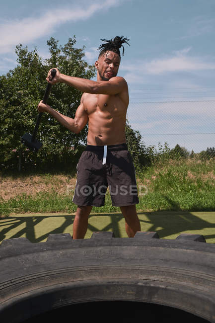 М'язистий чорний хлопець забиває шину у відкритому тренажерному залі — стокове фото