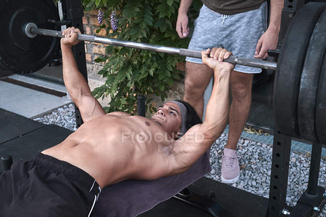 Ethnic man lifting barbell with trainer — Stock Photo