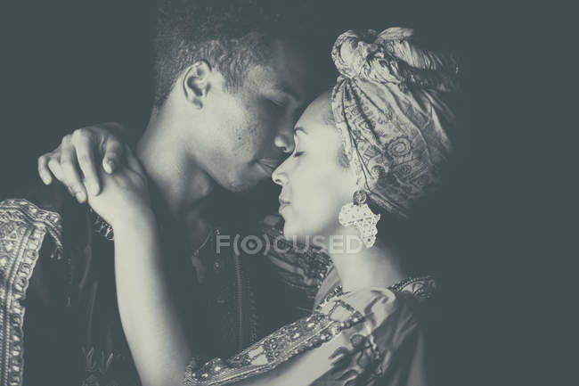Joven pareja africana atractiva en ropa étnica brillante abrazo con los ojos cerrados - foto de stock