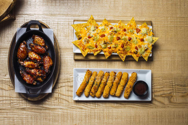 Сверху аппетитные жареное мясо хрустящие вкусные куриные палочки и ароматные сырные начос на столе — стоковое фото