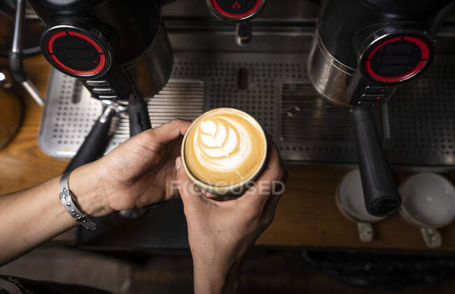 From above crop hands of professional employee preparing cappuccino with pattern on top in coffee shop — Stock Photo