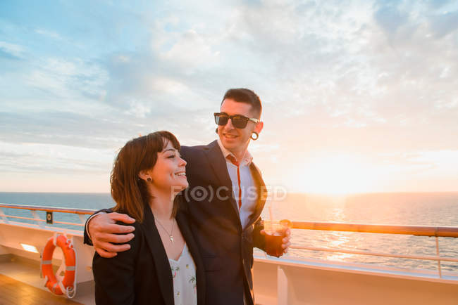 Jovem casal atraente beber bebida vermelha com palhas de um copo no fundo do mar por do sol — Fotografia de Stock