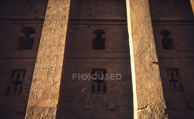 Antigua iglesia tallada en roca exterior con ventanas talladas y cruces en piedra, Etiopía - foto de stock