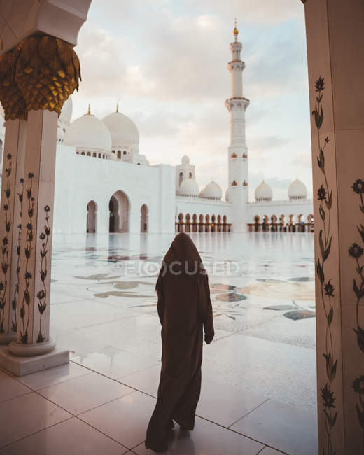 Visão traseira da mulher islâmica anônima em vestido preto longo andando na praça de azulejos da majestosa mesquita branca, Dubai — Fotografia de Stock