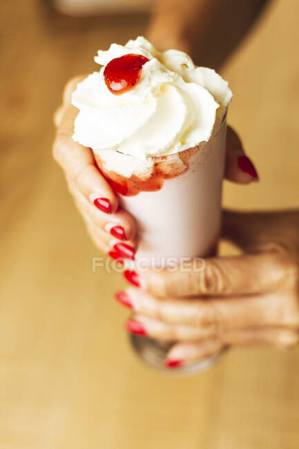 From above tasty ice cream decorated with red juicy in paper cone in hands with ideal manicure — Stock Photo