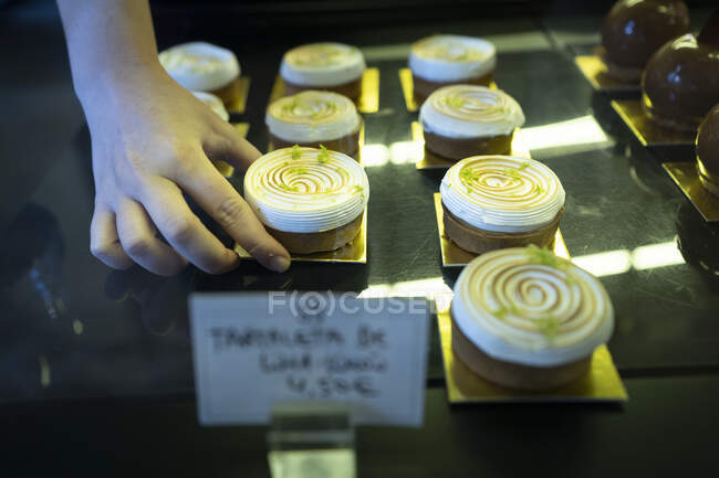 Unrecognizable person hands holding a delicious meringue cake into a bakery display — Stock Photo