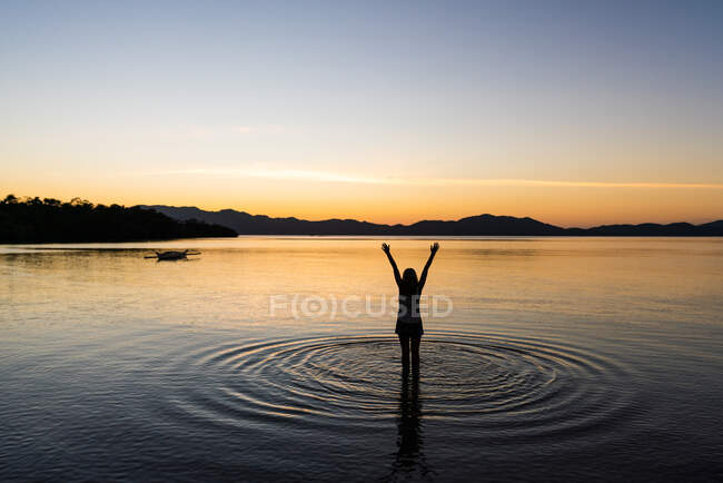 Vista posteriore della giovane donna in piedi in acqua con le mani alzate e godendo di una vista pittoresca sull'estate — Foto stock