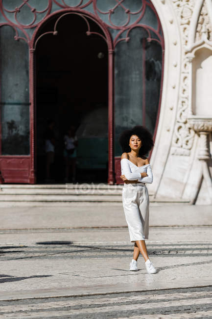 Приваблива модна жінка в білих штанях і верхньому посіві, що стоїть щасливо в літній день на міському фоні — стокове фото