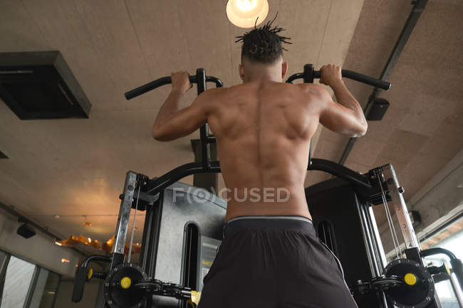 Muscular guy doing pull ups on exercise machine — Stock Photo