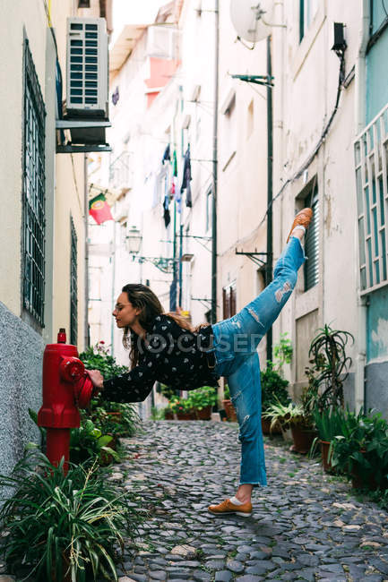 Joven mujer esbelta casual que se extiende en la calle de la ciudad vieja mientras baila con gracia - foto de stock