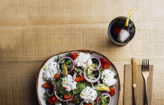 Ensalada de verduras con verduras de cebolla y salsa de crema servida en plato sobre mesa de madera - foto de stock