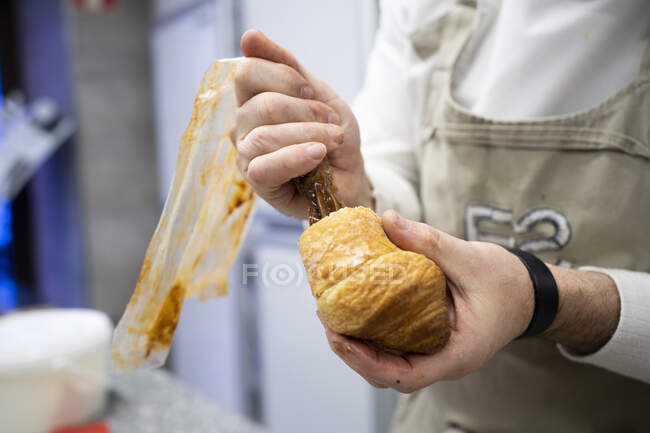 Crop man in grembiule e bianco uniforme imbottitura croissant fresco con crema di cioccolato in casa — Foto stock