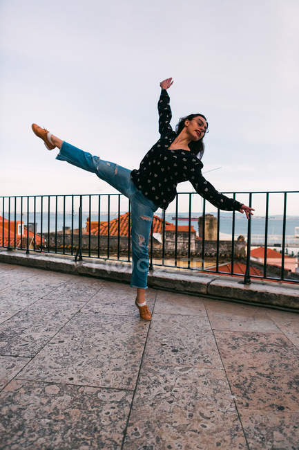 Casual young woman flying in splits while dancing on background of coastal city — Stock Photo