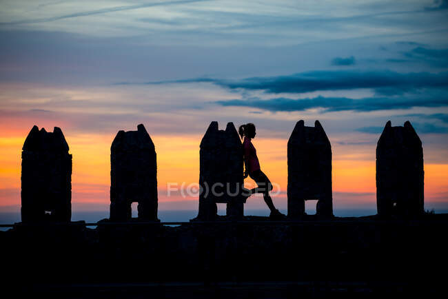 Silhueta de mulher irreconhecível apoiada em esculturas de pedra retangulares no céu sombrio de tirar o sol — Fotografia de Stock