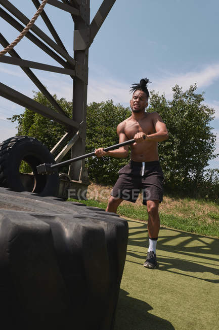 Muscular black guy hammering tire in outdoor gym — Stock Photo