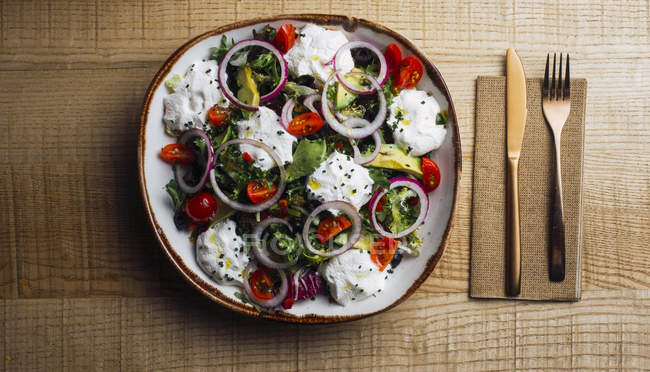 Ensalada de verduras con verduras de cebolla y salsa de crema servida en plato sobre mesa de madera - foto de stock