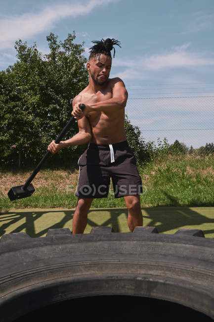 Muscular preto cara martelando pneu no ginásio ao ar livre — Fotografia de Stock