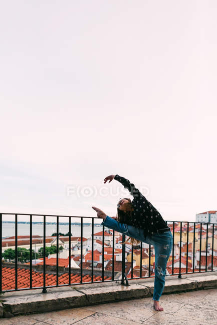 Casual young woman dancing on background of coastal city — Stock Photo