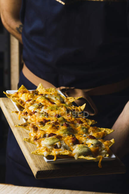 De arriba apetitoso asado crujiente sabroso queso nachos en el plato en manos del hombre - foto de stock