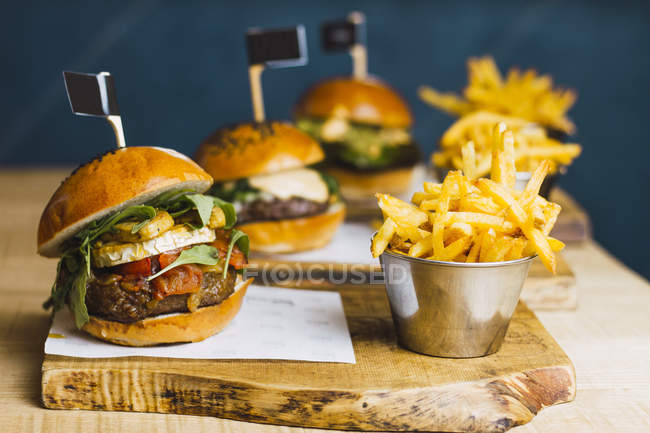 Deliciosos hambúrgueres suculentos e batata frita na mesa de madeira — Fotografia de Stock