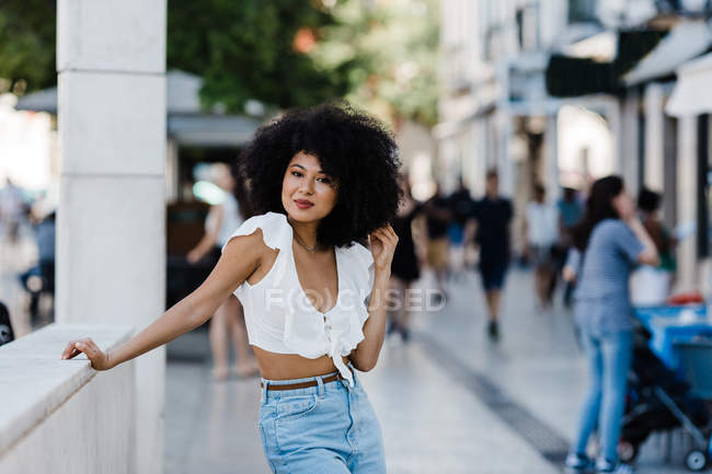 Junge afrikanisch-amerikanische Frau in Jeans und bauchfreiem Oberteil lehnt entspannt an einem Steingeländer und blickt in die Kamera im Freien — Stockfoto