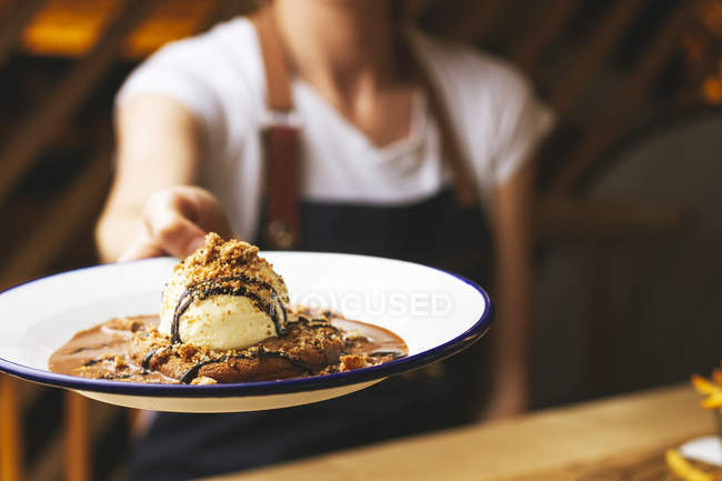 Hand of chef holding tasty sweet burger with chocolate crumb and nuts served on plate — Stock Photo