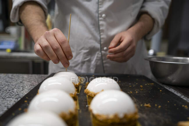 Erntehelfer stecken Holzstäbchen in Kuchen, die in der Küche auf Metallbrettern angeordnet sind — Stockfoto