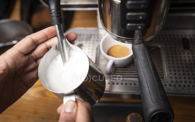 Сверху руки профессионального работника готовят капучино с узором сверху в кофейне — стоковое фото