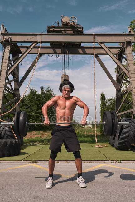 Muscular strong guy with barbell in outdoor gym — Stock Photo