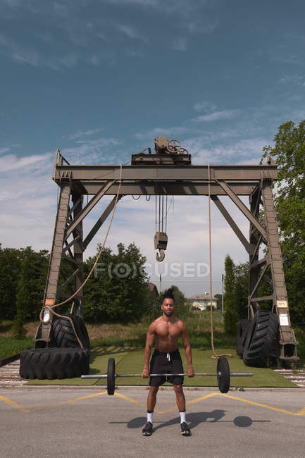 Hombre afroamericano despiadado que levanta una cortina pesada mientras hace ejercicio en el gimnasio al aire libre. - foto de stock