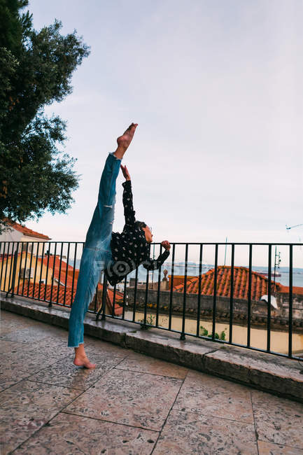 Casual young woman flying in splits while dancing on background of coastal city — Stock Photo