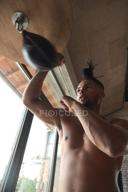 From below shirtless African American guy punching bag during boxing workout in gym — Stock Photo