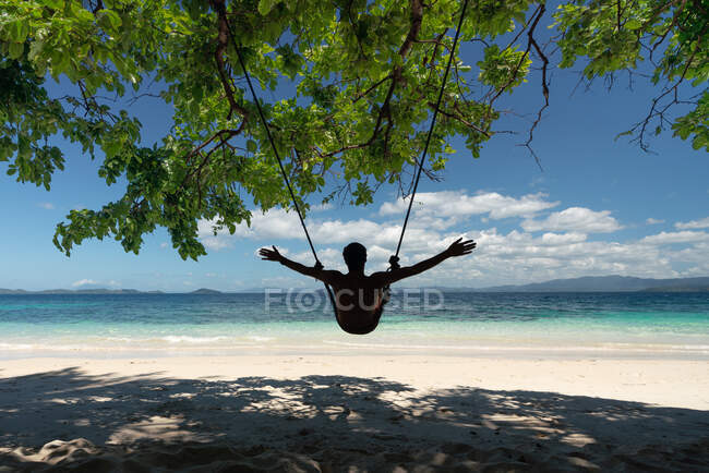Rückansicht des Reisenden entspannt sich auf Schaukel und bewundert malerische Aussicht, während er sich am Sandstrand ausruht — Stockfoto