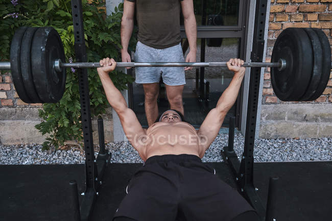 Тяжелоатлет поднимает штангу с тренером — стоковое фото