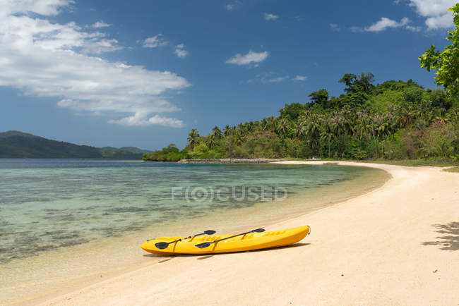 Пустое желтое каноэ на песчаном пляже тропического острова на фоне джунглей и голубого неба — стоковое фото
