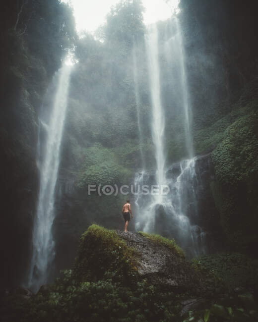 Turista su roccia sotto cascata nebbiosa — Foto stock