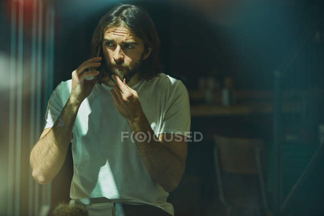Молодой бородатый красивый мужчина в кафе за окном разговаривает по телефону — стоковое фото