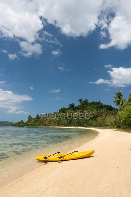 Empty yellow canoe on sandy beach of tropical island on background of jungle and blue sky — Stock Photo