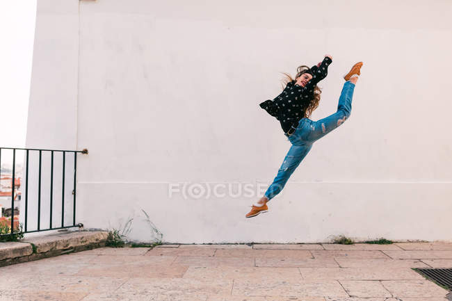 Lässige junge Frau fliegt im Spagat, während sie auf dem Hintergrund der weißen Wand tanzt — Stockfoto