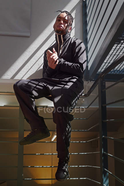Young African American man sitting on metal handrails and looking at camera — Stock Photo