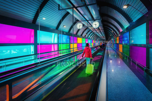 Невпізнанний жінка з валізою їзда косіння доріжки біля барвистих панелей усередині аеропорту Мадрид Барахас в Іспанії — стокове фото