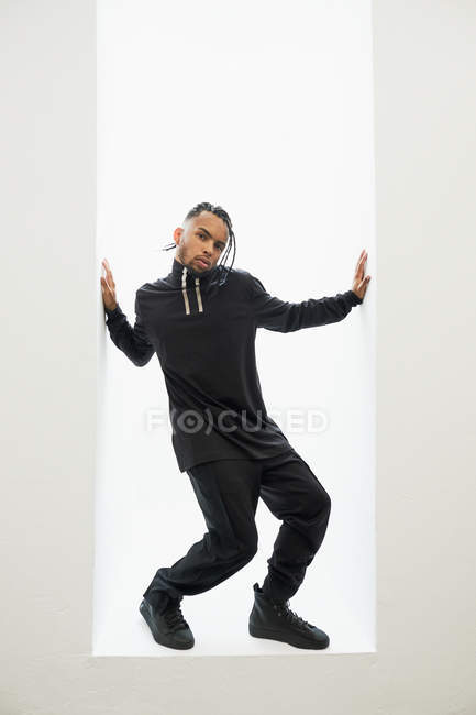 Hombre afroamericano en ropa negra con pelo trenzado posando sobre fondo blanco - foto de stock