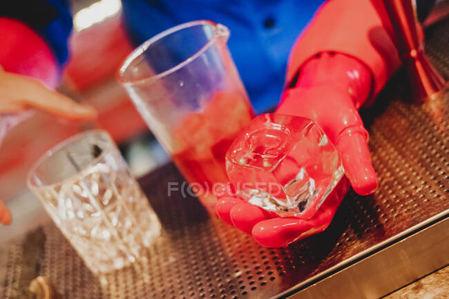З вище великого прямокутного кубика льоду в руці бармена в уніформі і червоних рукавичках — стокове фото