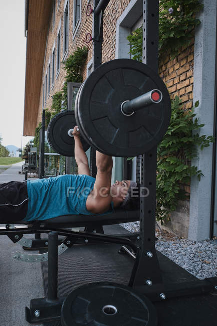 Side view of strong guy lifting barbell on street — Stock Photo