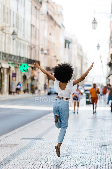 Back view of happy ethnic woman in trendy outfit jumping for joy on summer day — Stock Photo