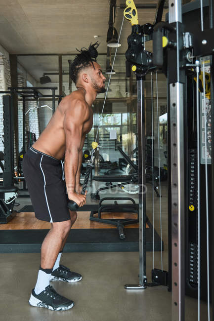 Black guy using exercise machine in gym — Stock Photo