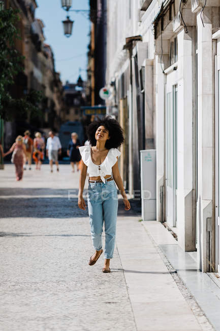 Mulher na moda atraente em jeans e top de cultura desfrutando de caminhada no dia de verão em fundo urbano desfocado — Fotografia de Stock
