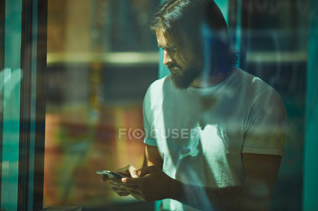 Jeune homme beau barbu appuyé sur le mur avec téléphone portable dans les mains textos réfléchis — Photo de stock