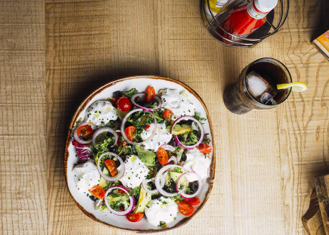Gemüsesalat mit Zwiebelgemüse und Sahnesoße auf Teller auf Holztisch serviert — Stockfoto